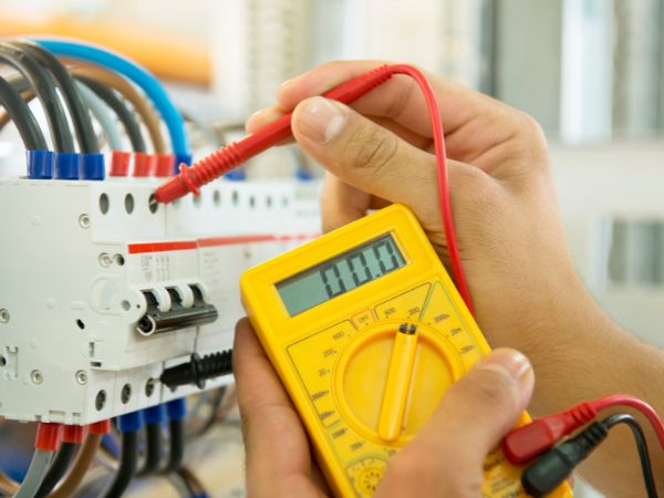 Un technicien en train de vérifier le bon fonctionnement d'un coffret électrique en utilisant un voltmètre à la main.